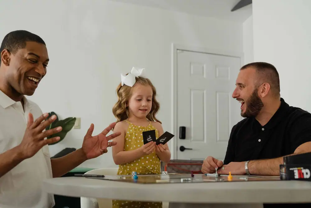 Two adults and a young child laughing while playing a card game at home