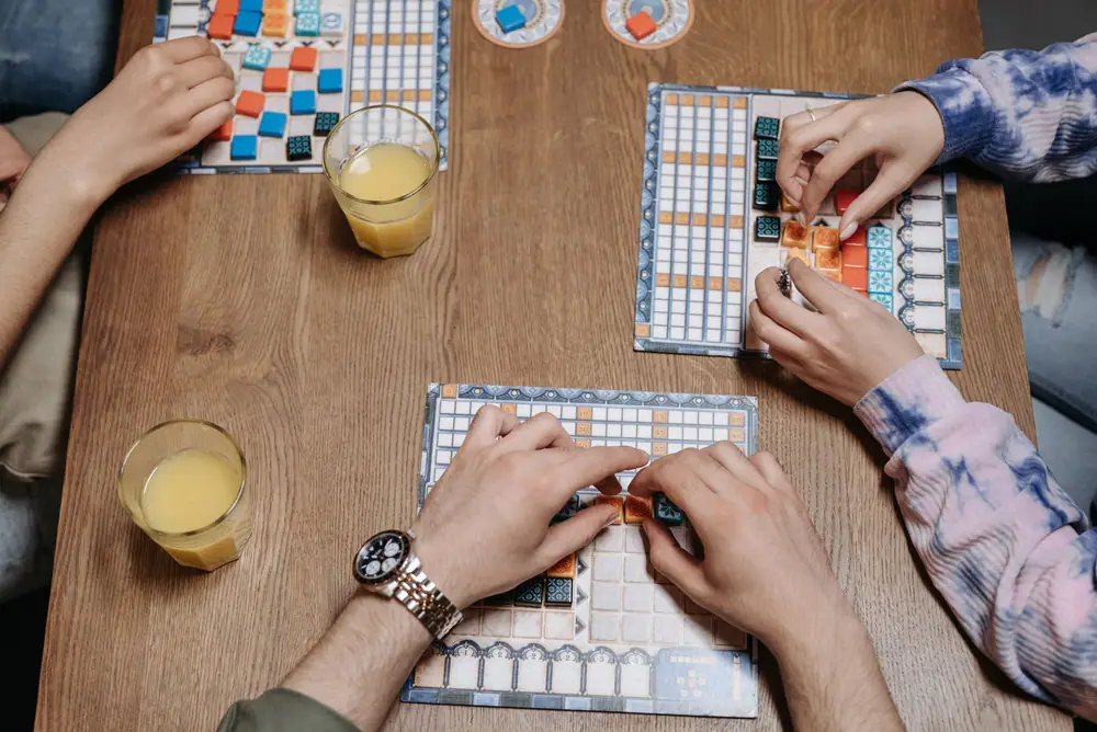 Players placing colorful tiles on boards during a tabletop game