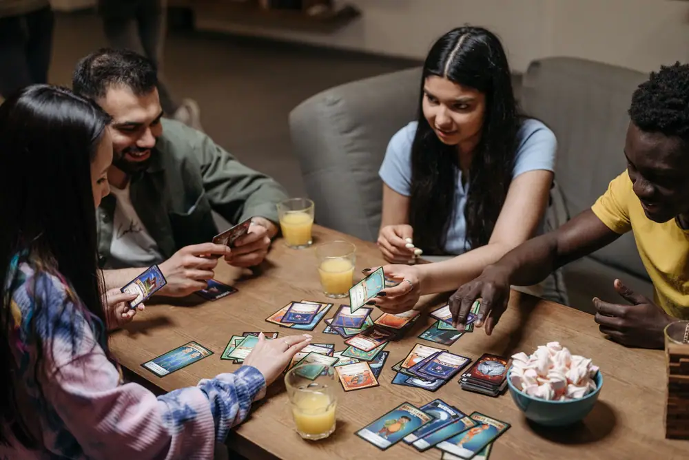 Friends laughing while playing a card game around a wooden table