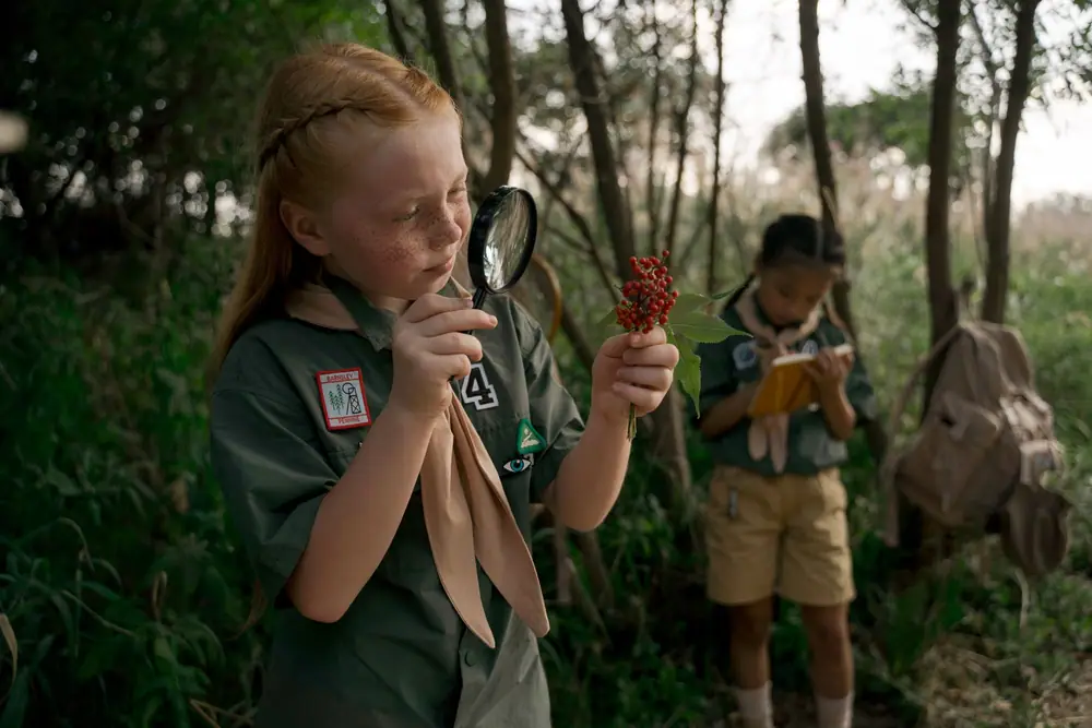 A child in a scout uniform looks through a magnifying glass during an outdoor hunt